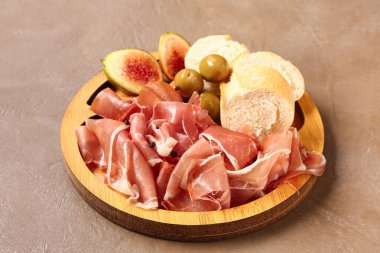 Lezzetli prosciutto dilimleri ve kahverengi arka planda ekmeği olan ahşap tahta tahta.