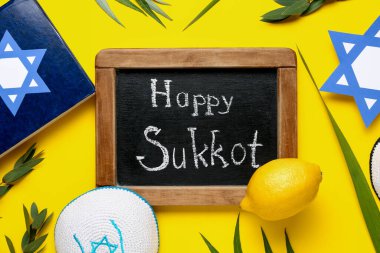 Dört tür (lulav, hadas, arava, etrog) ve sarı arkaplanda Mutlu SUKKKOT yazılı kara tahta