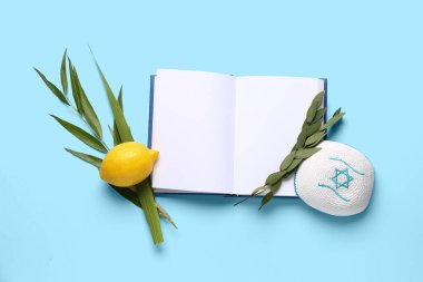 Dört tür (lulav, hadas, arava, etrog) Sukkot festival sembolleri, kippah ve mavi arkaplan üzerine boş sayfaları olan açık kitap