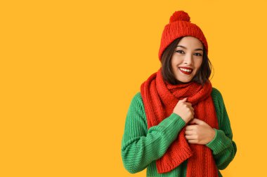 Sarı arka planda, kalın giysili güzel Asyalı kadın.