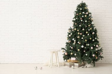 Beyaz tuğla duvarın yanında mücevher ve hediye kutuları olan Noel ağacı
