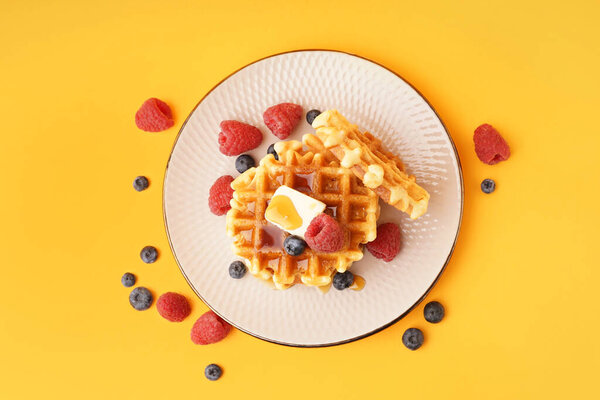 Plate of tasty waffles with berries and maple syrup on yellow background