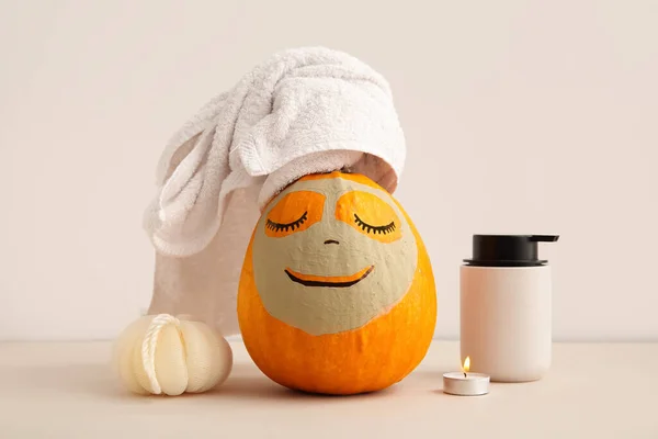 Pumpkin with clay mask and bath supplies on beige background