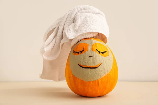 Pumpkin with drawn face, clay mask and towel on beige background