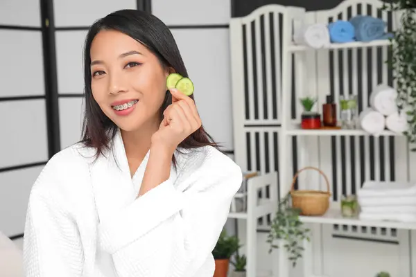 Young Asian woman with cucumber slices at home