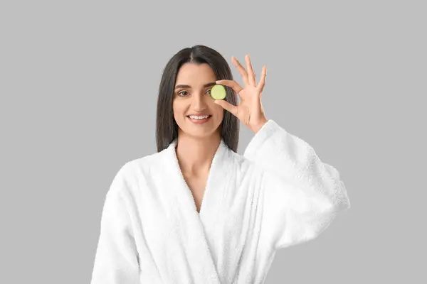 Young woman with cucumber slice on light background