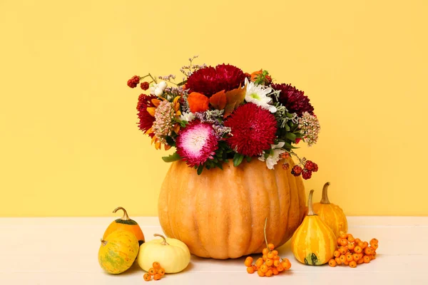 Beautiful autumn bouquet in pumpkin on white wooden table against yellow background