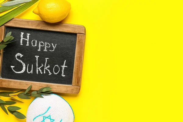 stock image Four species (lulav, hadas, arava, etrog) and chalkboard with text HAPPY SUKKOT on yellow background