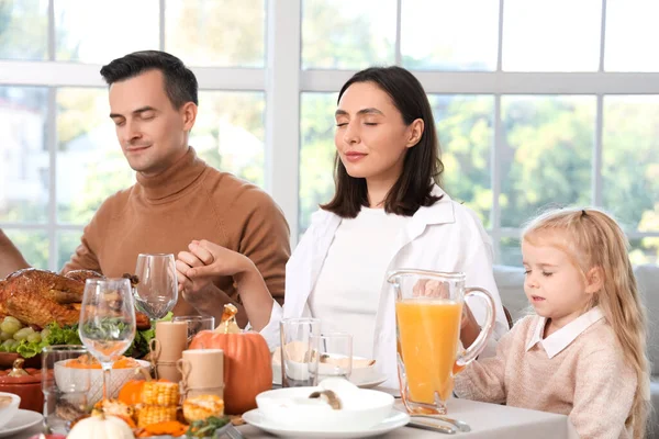 Happy family praying before dinner at festive table on Thanksgiving Day