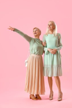 Pembe arka planda güzel, şık olgun kadınlar.