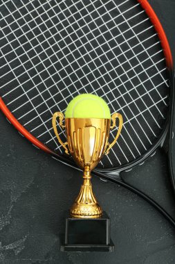 Koyu arkaplanda top ve tenis raketi olan altın bardak.