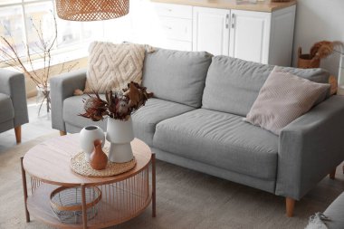 Oturma odasında kurutulmuş protea çiçekleri olan rahat gri kanepe ve kahve masası.