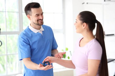 El ele tutuşan erkek fizyoterapist ve rehabilitasyon merkezinde genç bir kadın.