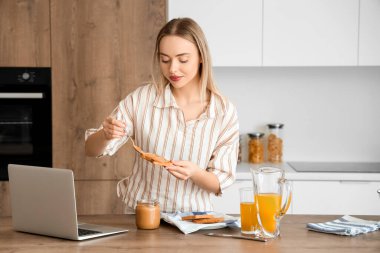 Genç bir kadın mutfakta tostun üzerine fıstık ezmesi sürüyor.