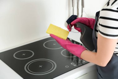 Pembe lastik eldivenli kadın elektrikli ocağı sünger ve deterjanla temizliyor.