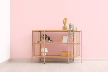 Odada pembe duvarın yanında çiçek ve dekor bulunan modern raf ünitesi.