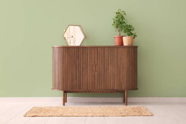 Çağdaş çekmeceler, içinde ev bitkileri ve yeşil duvarın yanındaki ayna.