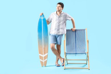 Mavi arka planda sörf tahtası ve şezlonglu genç adam.