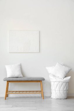 Beyaz duvarın yanında yastıklı gri bank ve sepet