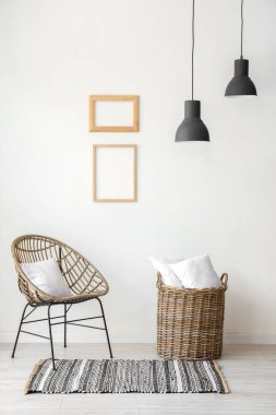 Beyaz duvarın yanında yastıkları olan hasır koltuk ve sepet.