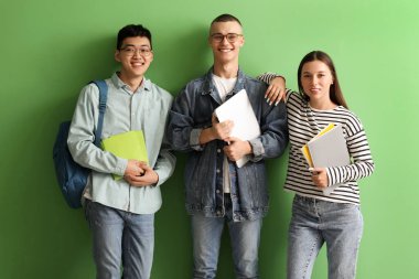 Yeşil arka planda dizüstü bilgisayarı olan mutlu öğrenciler.