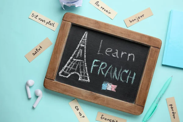 Chalkboard with text LEARN FRENCH, stationery and earphones on blue background