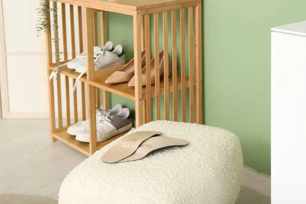 Orthopedic insoles on stool and shoe rack with shoes near color wall