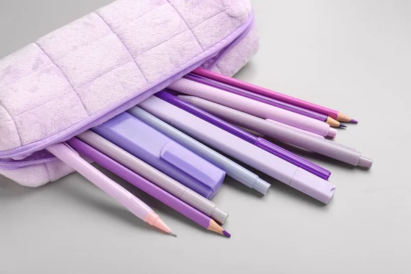 Purple pencil case with school stationery on grey background, closeup
