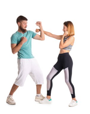 Beyaz arka planda kendini savunma eğitmeniyle kavga eden genç kadın.