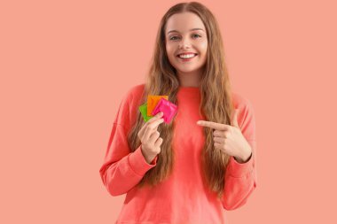 Pembe arka planda prezervatifleri gösteren genç bir kadın.