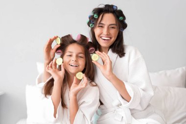 Küçük kız ve annesi salatalık dilimleri ile yatak odasında kıvırcık saçlar