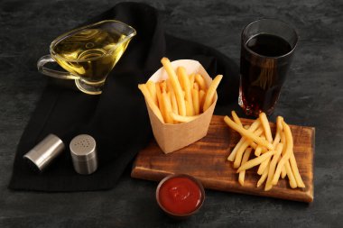 Lezzetli patates kızartması, kola, bir kase ketçap ve siyah arka planda baharatlar.