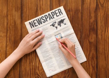 Gazetede tahta arka planda kalem işaretleyen kadın