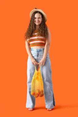 Turuncu arka planda mandalina dolu bir torba ile güzel bir genç kadın.