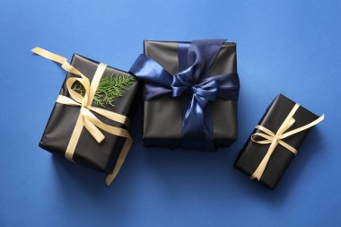 Mavi arka planda kozalaklı dalları olan siyah Noel hediye kutuları