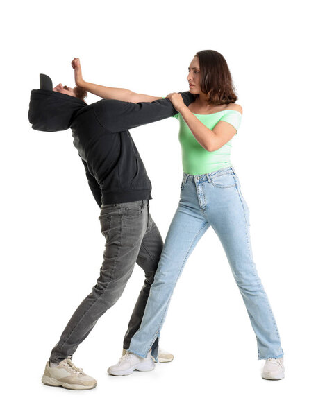 Young woman defending herself against robber on white background