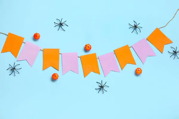 Garland made of paper flags, pumpkins and spiders for Halloween celebration on blue background