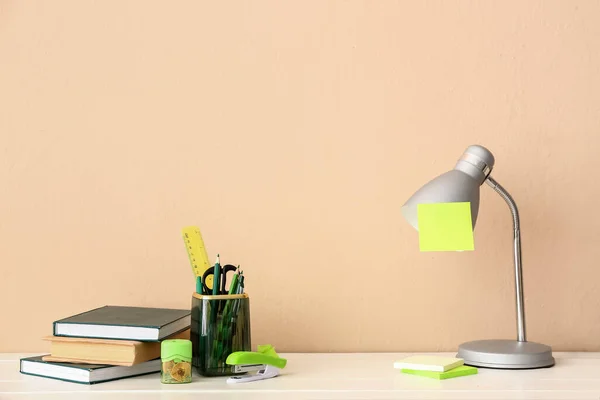 Holder with different stationery, books and lamp on light wooden desk