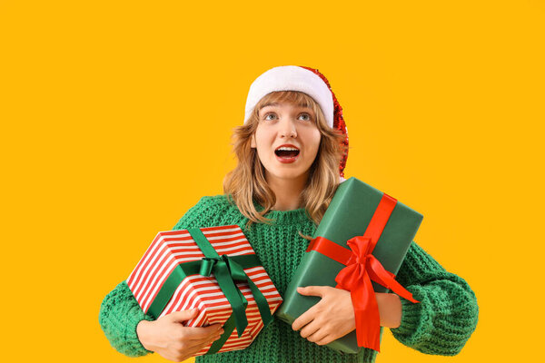 Young woman in Santa hat with Christmas presents on yellow background