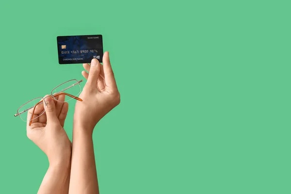 Woman with credit card and eyeglasses on green background