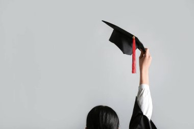 Gri arka planda mezuniyet şapkası olan kadın.
