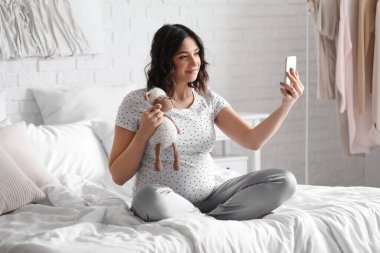 Yatak odasında cep telefonu kullanan hamile bir kadın.