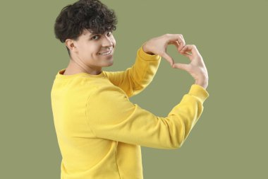 Yakışıklı genç adam, elleri yeşil arka planda kalp yapıyor.