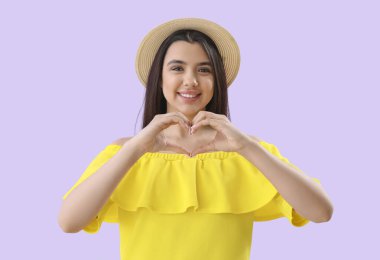 Elleri leylak arkaplanda kalp yapan genç bir kadın.