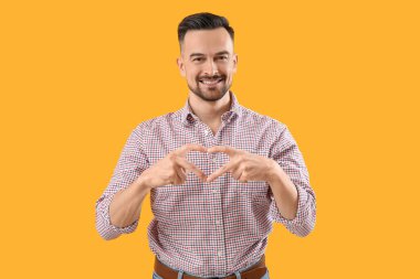 Yakışıklı adam, elleri sarı arka planda kalp yapıyor.