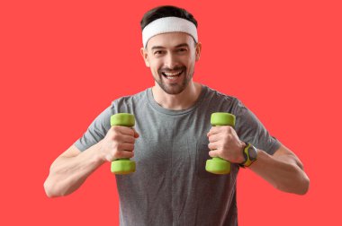 Kırmızı arka planda dambılları olan sportif bir genç.