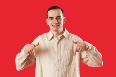 Genç adam kırmızı arka plandaki bir şeyi işaret ediyor.