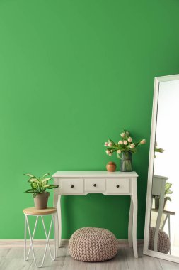 Yeşil duvarın yanında lale çiçekli ve şık aynalı bir masa.