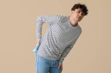 Bej arka planda sıcak su şişesiyle sırtını ısıtan genç bir adam.