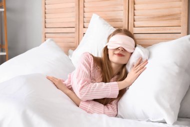 Yatakta yastıkların üzerinde uyuyan maskeli genç bir kadın.